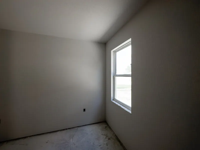 An empty room stripped of furniture, with a bare unfinished floor and a single uncurtained window